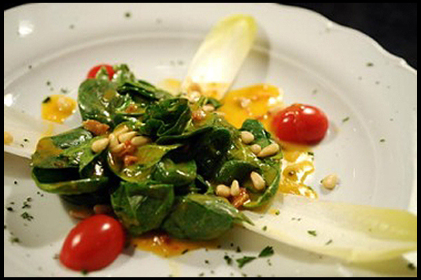 Baby Spinach Tossed in a Warm Bacon, Potato Dressing and Garnished with Pine Nuts, Endive Leaves and Tomatoes.