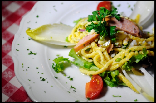 Spätzle tossed with Green Peas, Red Onions and Smoked Bavarian Sausage in a Home-Made Riesling Dressing garnished with Salad Greens and Tomatoes.